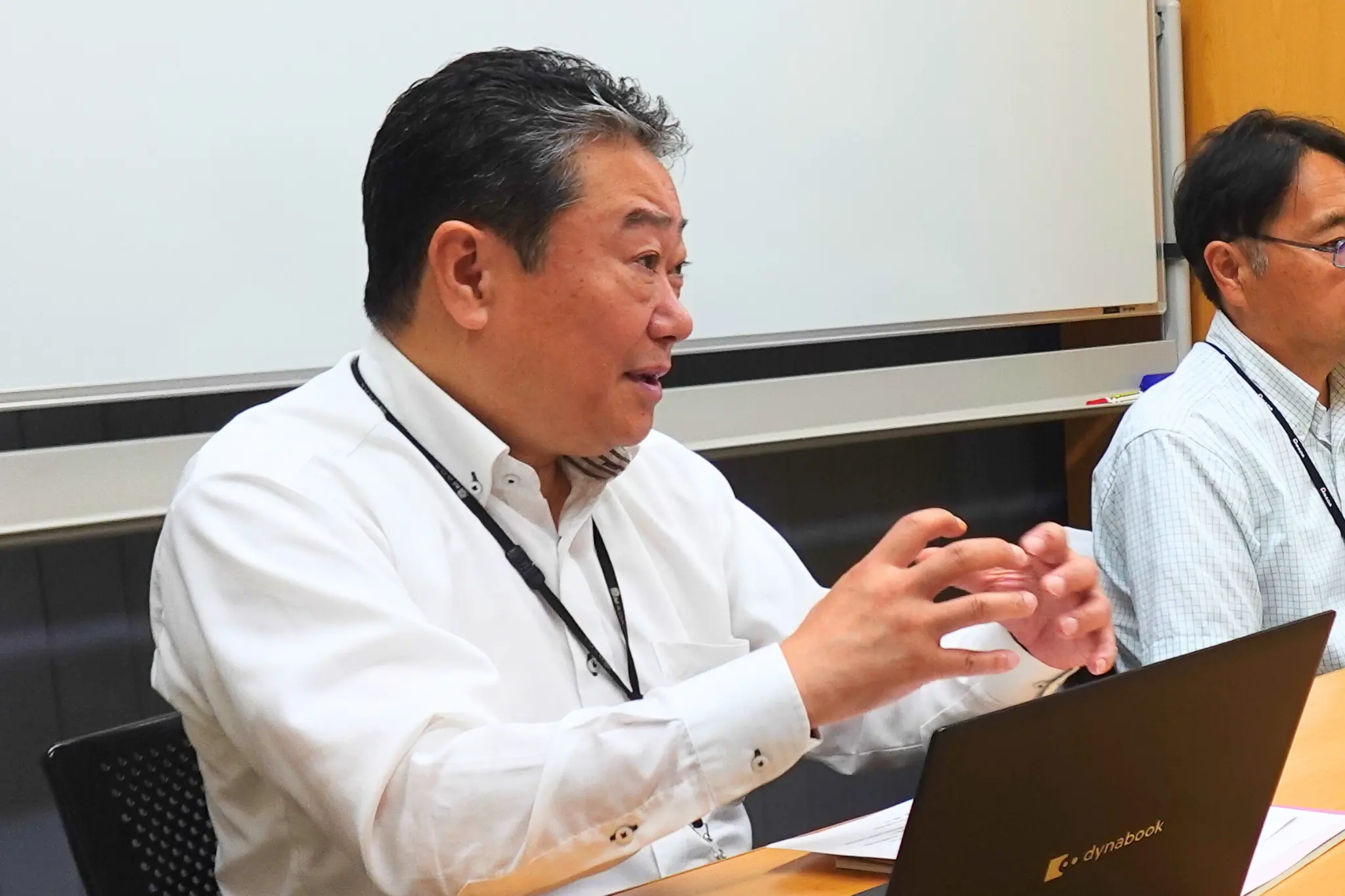 会議室で担当者がノートPC前で発言する様子。化学物質情報管理の課題や導入効果について語るインタビューシーン。