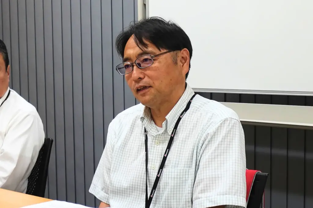 会議室で担当者が発言するインタビューシーン。運用面の使い勝手や社内展開の手応えを述べるシーン。