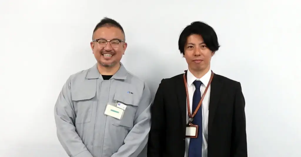 作業服姿とスーツ姿のユーザー企業担当者2名が並んで笑顔でカメラを見ているツーショット写真