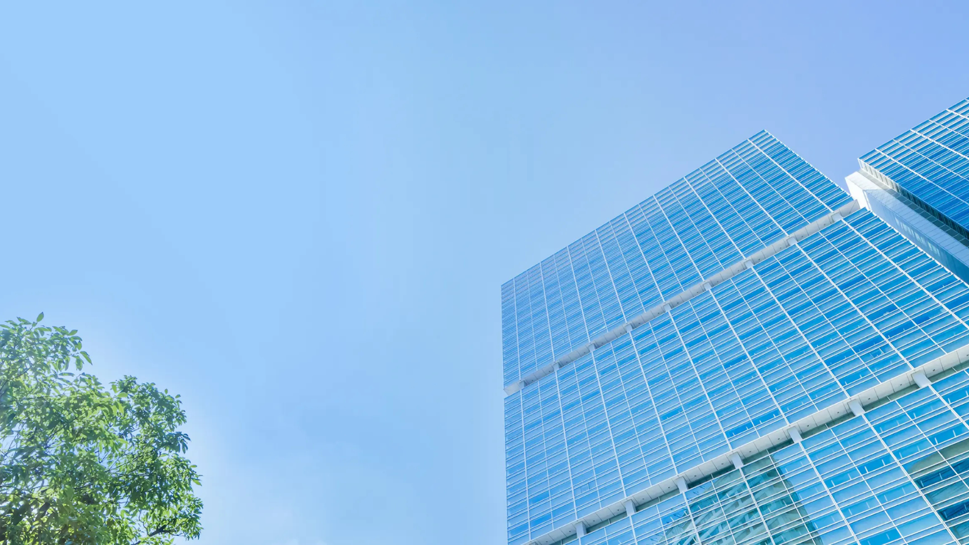 ガラス張りの高層オフィスビルと青空、左下に緑の街路樹を配した事業所・サービス拠点紹介ページ用カバー画像。