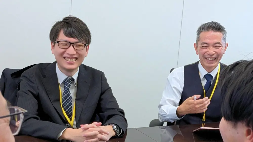 ユニプレス株式会社の担当者2名がテーブル越しに笑顔で打ち合わせしている会議風景の写真