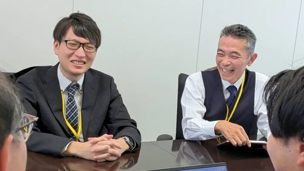 ユニプレス株式会社の担当者2名がテーブル越しに笑顔で打ち合わせしている会議風景の写真