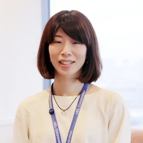 IDストラップを着け笑顔で立つ女性社員のバストアップ。