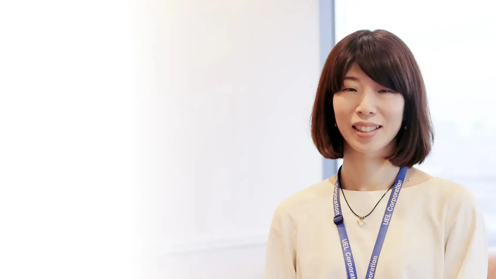 女性社員インタビューのトップビジュアル。明るいオフィス空間を背景に笑顔で立つ木村さんの上半身。