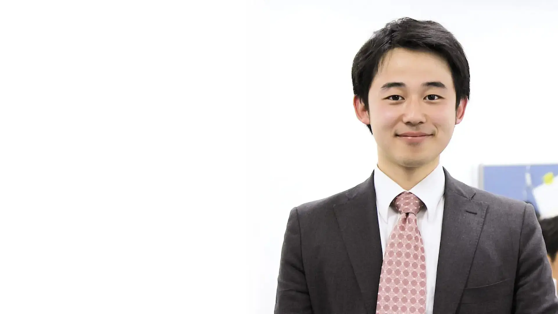 オフィスでスーツ姿の若手男性社員が微笑む、社員インタビュー記事のトップイメージ