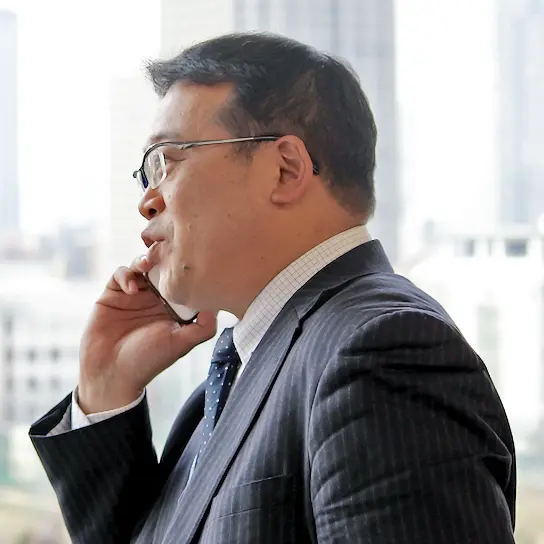 窓際でスマートフォン通話中の男性社員横顔。