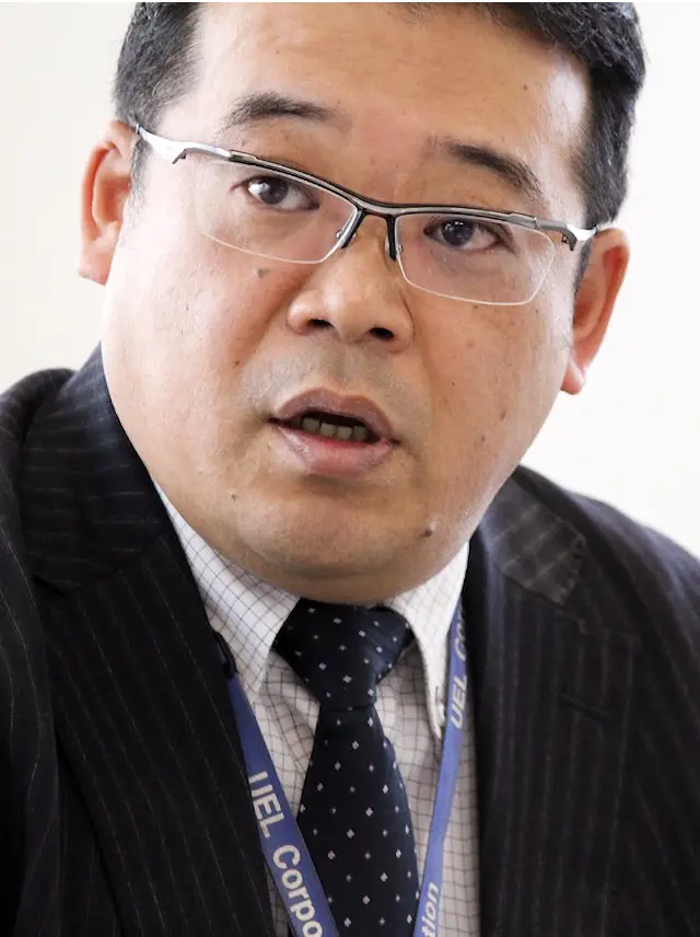 真剣な眼差しで語る坂本さんのクローズアップ。UELのネームストラップが胸元に光り、臨場感がある。