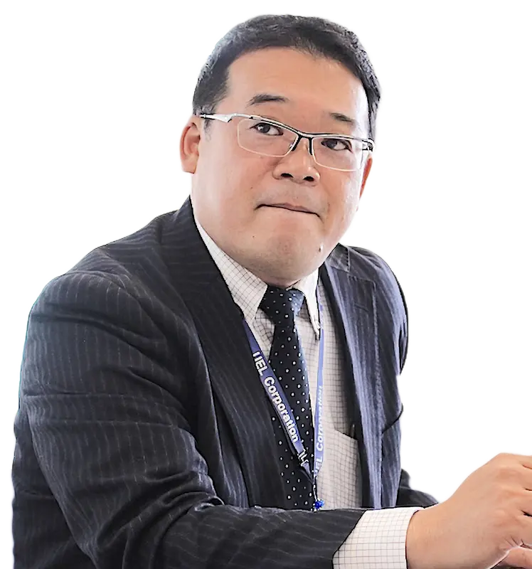 背景透過の全身ポートレート。着席姿勢でネームカードを下げた坂本さんが穏やかにこちらを見つめる。