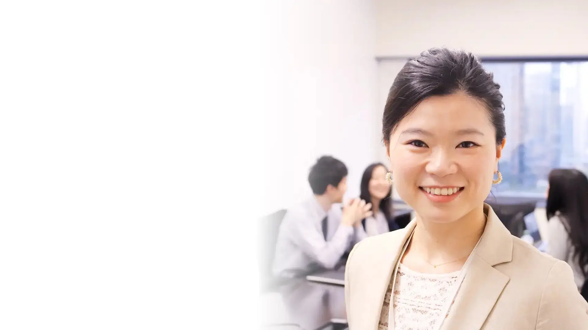 インタビュートップ画像。左に余白、右側に住吉さんが立ち、後方に談笑する社員たち。