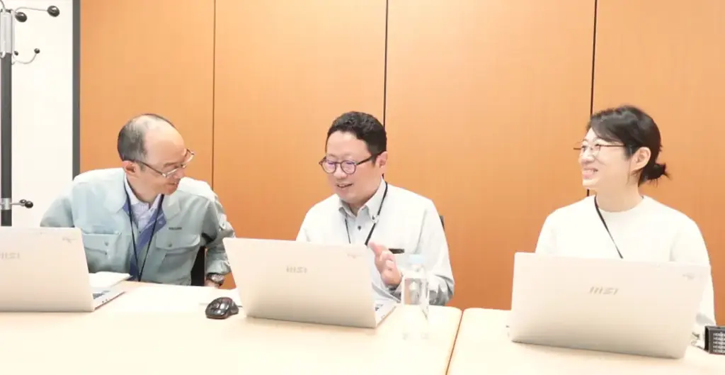 加賀マイクロソリューションの担当者3名がノートPCを囲み笑顔で談笑しながらグリーン調達マイスター活用を振り返る様子。